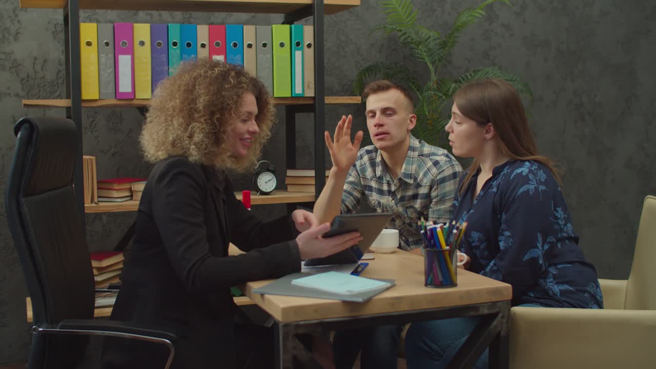 una pareja enfocada con una agente inmobiliaria seleccionando opciones de vivienda en una tableta.