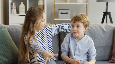 Zwei-Kleine-Süße-Kinder,-Schwester-Und-Bruder,-Sitzen-Auf-Dem-Sofa-Mit-Kissen-Im-Gemütlichen-Zimmer-Und-Umarmen-Sich-Vor-Der-Kamera