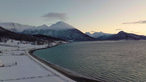 Polar-night-has-colorful-sky,-windy-conditions-over-ocean-with-snowy-mountains