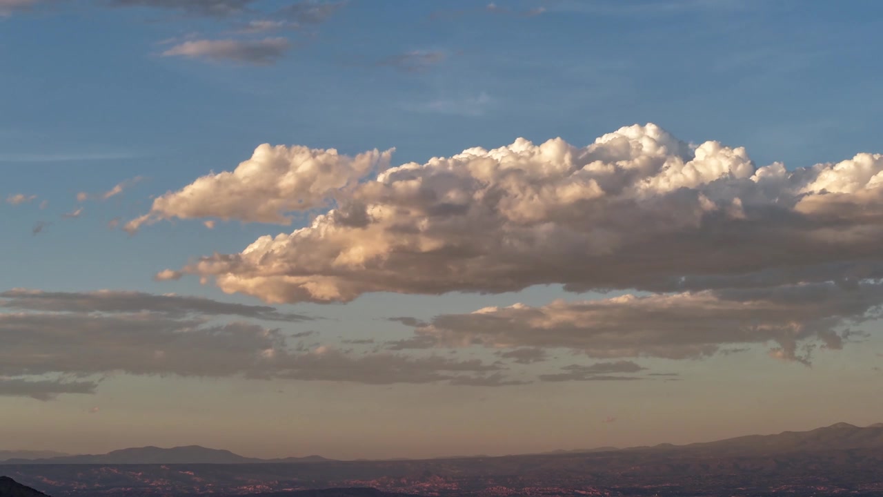 4K UHD drone timelapse: prominent isolated cumulus cloud drifts across vast southwestern desert sky. Shifting atmospheric weather highlights warm sunset tones and distant mountain ridges.