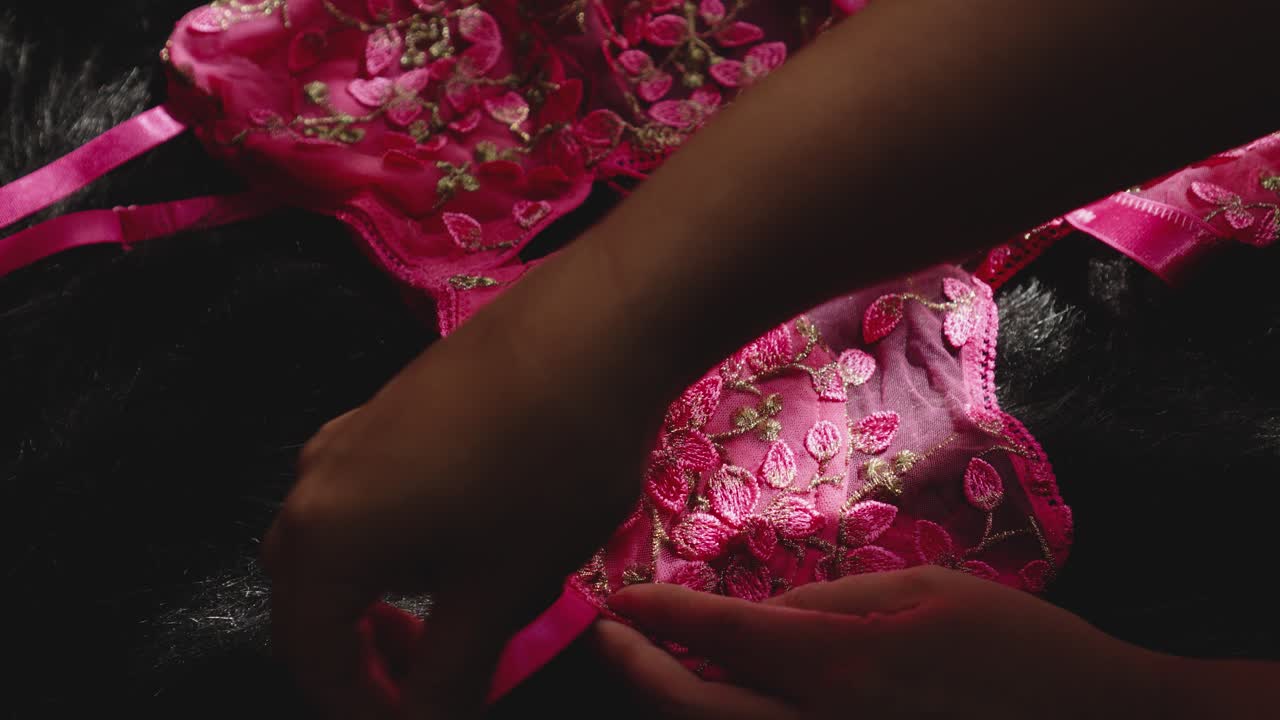 La mano di una donna accarezza la lingerie rosa prima di indossarla