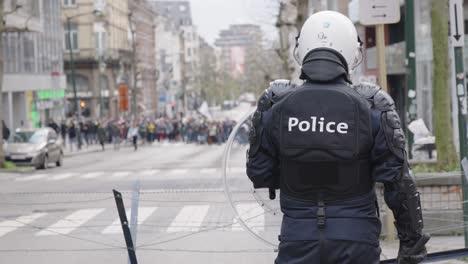 unrecognizable riot police officer protecting the city - view from behind back of cop, blurred background demonstration