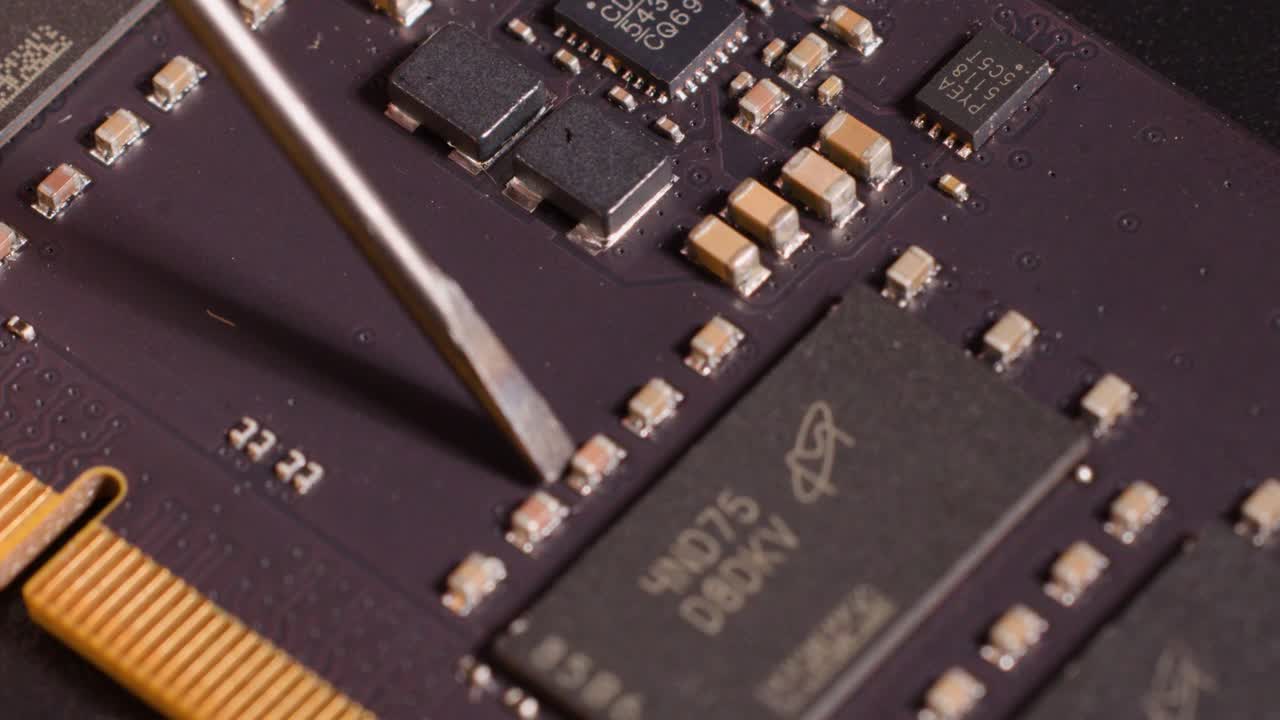 Macro close-up of a metal tool inspecting electronic components on a dark computer motherboard