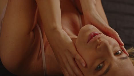 a sexy model lies in bed dressed in lingerie and sensually caresses her face in slow motion