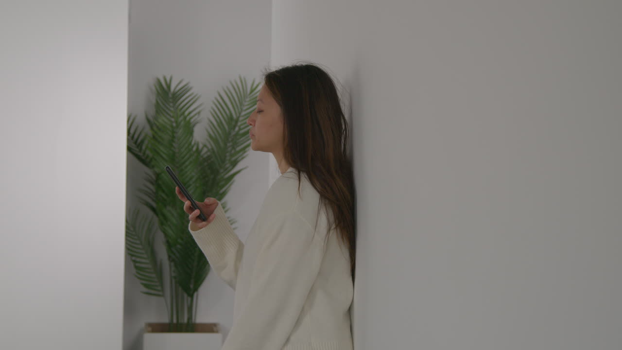 스트레스를 받거나 불안한 여성이 집에서 벽에 기대어 인터넷이나 소셜 미디어 뉴스 메시지 또는 휴대 전화에 반응합니다.