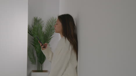 stressed or anxious woman leaning against wall at home reacting to internet or social media news message or story on mobile phone 3