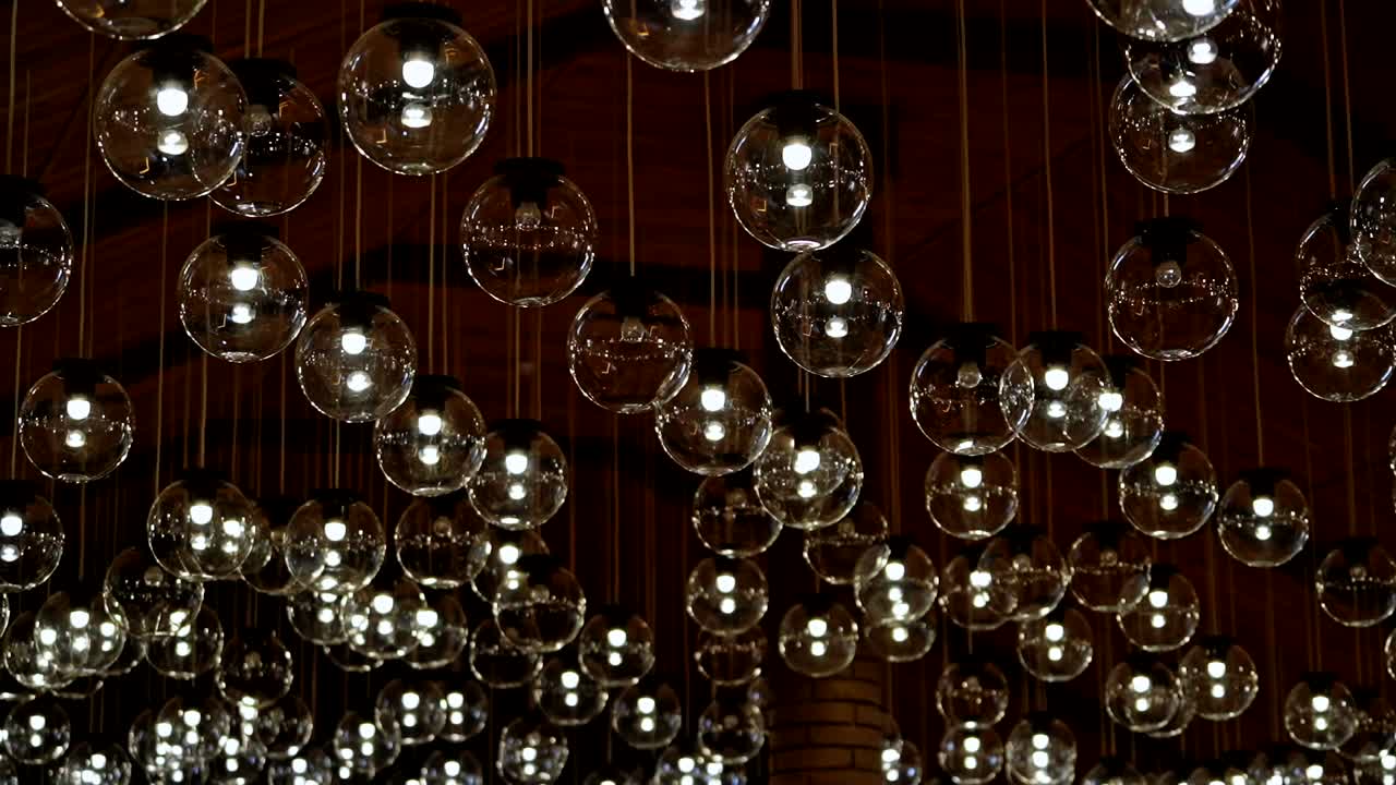 Many light bulbs lighting up. Dark background with lamps becomes bright. Beautiful ceiling with round glass lamps switches on.