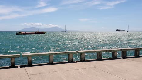 a view of tropical atauro island in the distance on the waterfront with ocean and moored boats in capital dili, timor leste, southeast asia