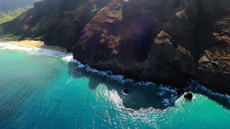 aerial view of blue coastline and crashing waves along rolling hills in kauai hawaii