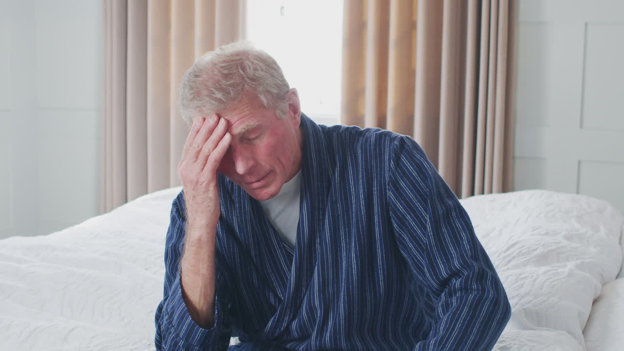 un anciano infeliz y deprimido sentado en el borde de la cama en casa durante el bloqueo por covid-19