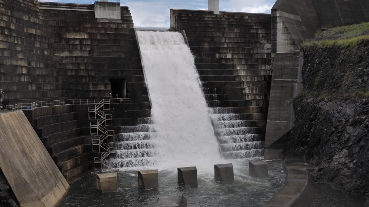 Wide view of water flowing through the Hinze Dam overflow and dam steps due to ongoing heavy rains in the Gold Coast Hinterland