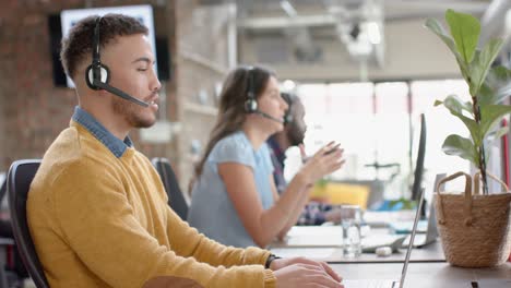 hombre de negocios biracial hablando por teléfono y usando una computadora portátil en la oficina