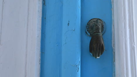 un primer plano de una puerta de puerta en forma de mano de época en una puerta azul desgastada en una antigua ciudad tunecina