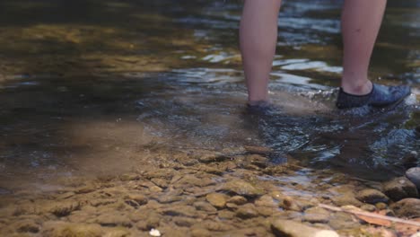 person's feet wearing water shoes walking through shallow stream, slow motion