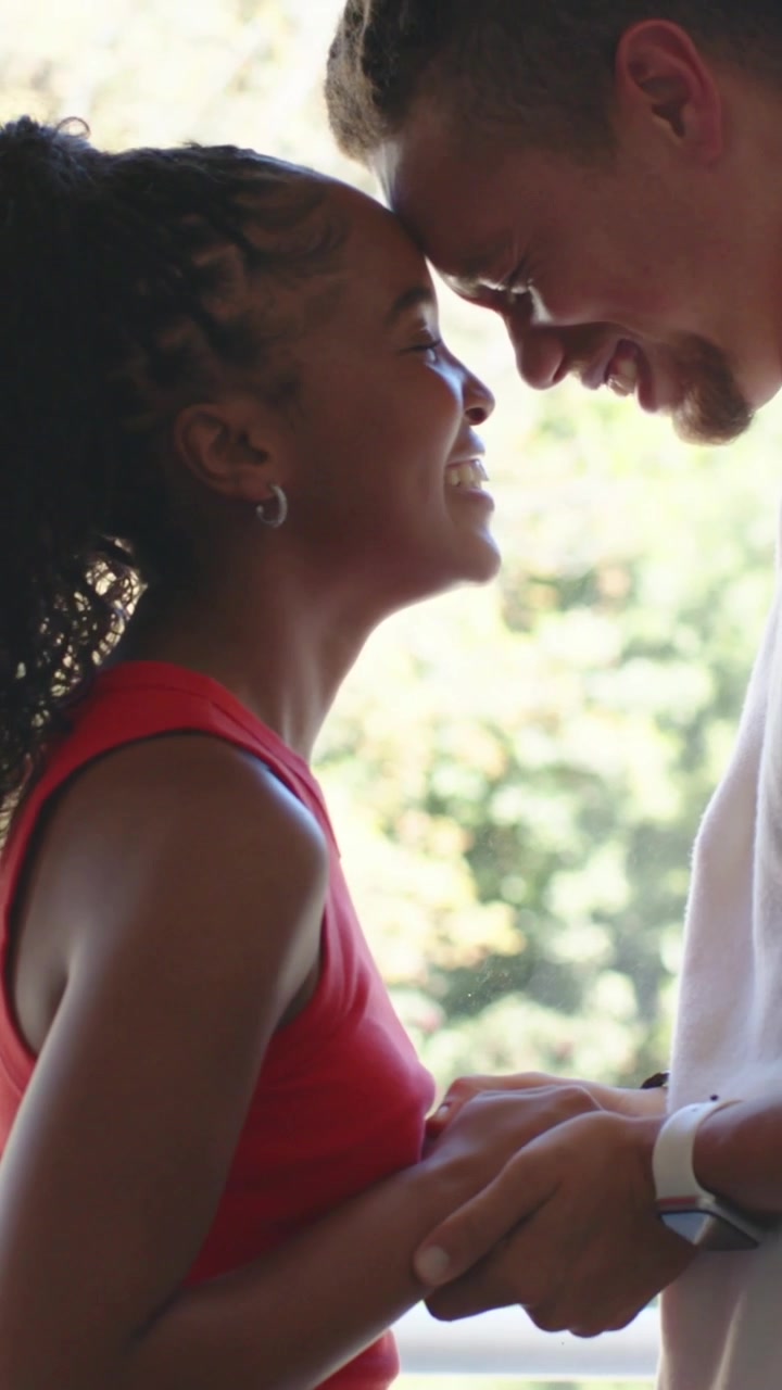 Vertical video: Laughing pair leaning in on porch, holding hands, sharing love, red top, white tee