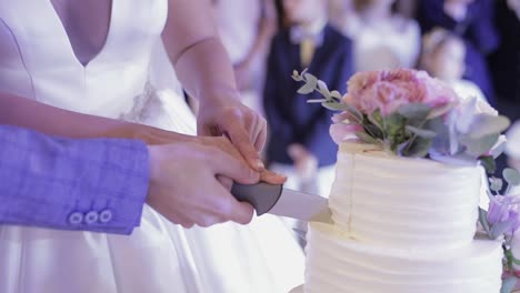 Bride-and-a-groom-is-cutting-their-wedding-cake.-Hands-cut-of-a-slice-of-a-cake