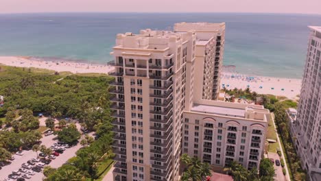 a drone shot with a jib-down motion descends over a beachfront hotel at sunset, capturing sandy shores, ocean waves, and the hotel’s sparkling pool under a golden sky.