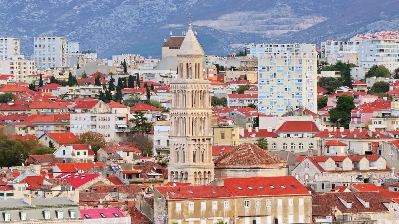 Aerial drone view of the iconic bell tower of Split rising above red rooftops with mountains in the background