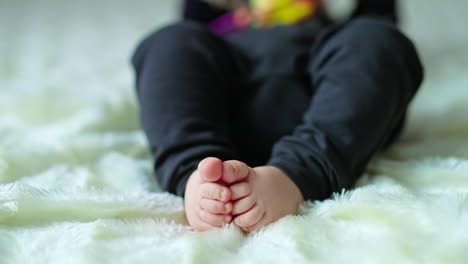 cute baby feet rubbing each other. child in dark clothes lies on the bed covered with white plaid. blurred backdrop.