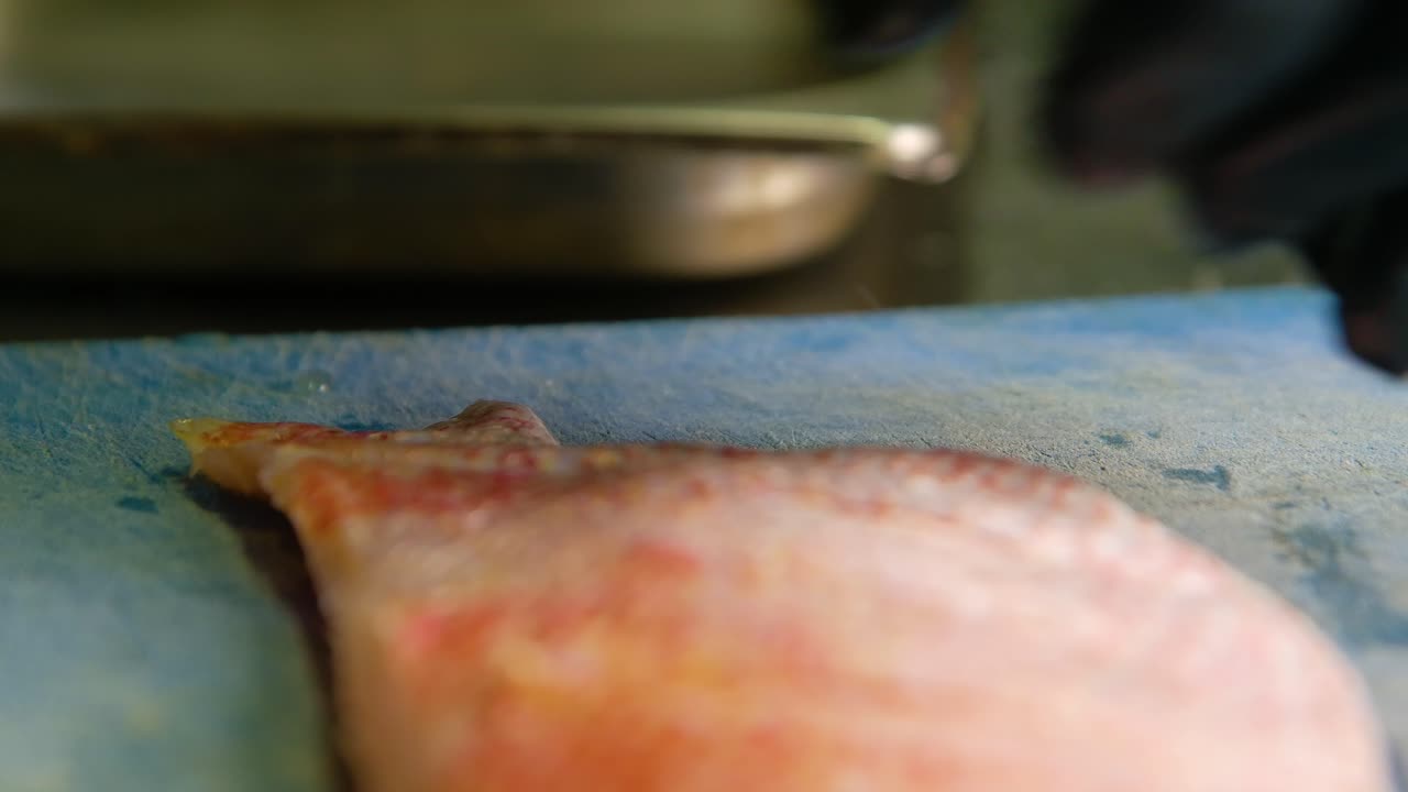 chef usando guantes de látex negro puntuaciones y rodajas a través de la piel de pescado filete de pargo rojo