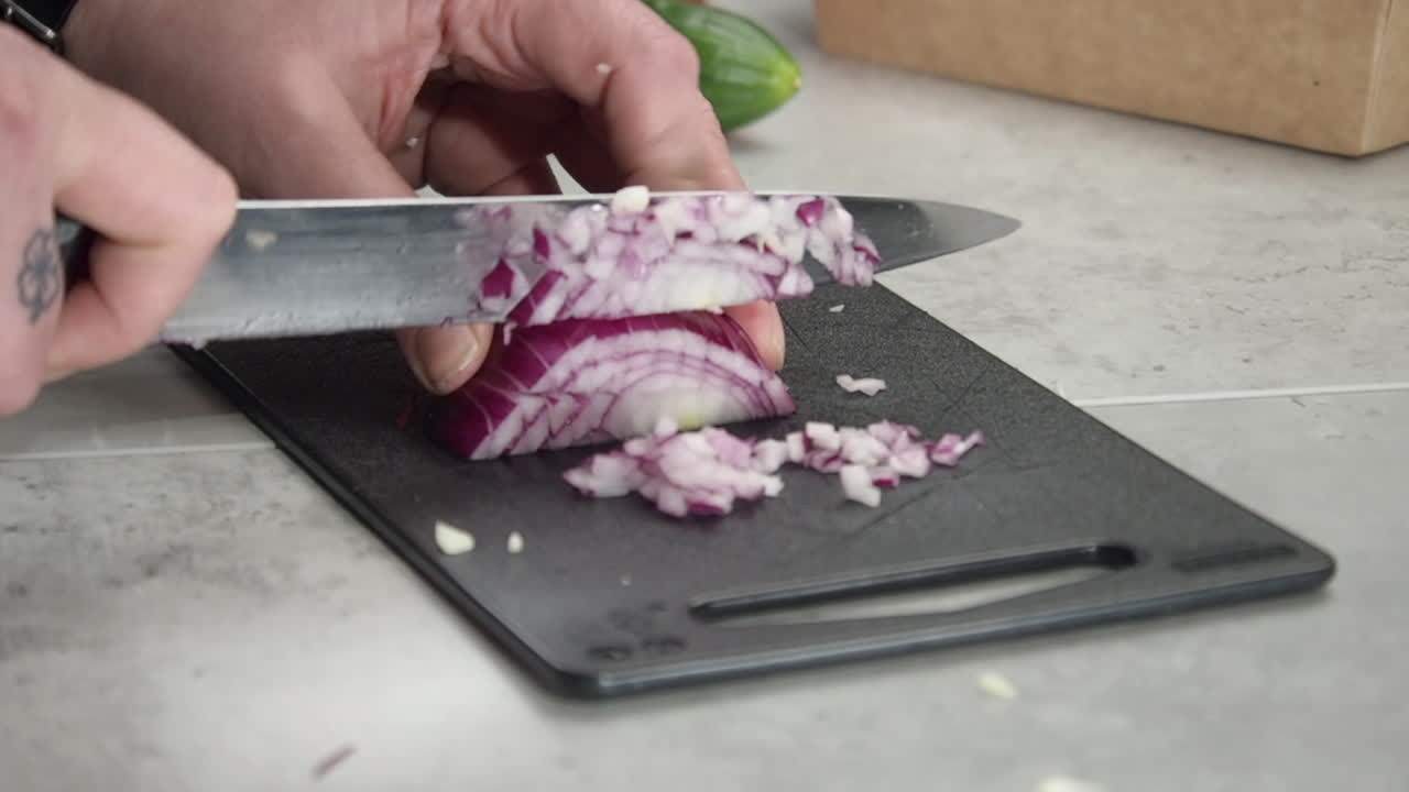 Kitchen cook uses knife to dice red onion into small pieces, closeup