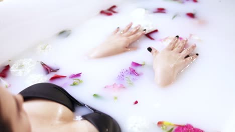 close up view of young attractive woman relaxing in milk bath filled with flowers. spa and skin care concept. slow motion shot