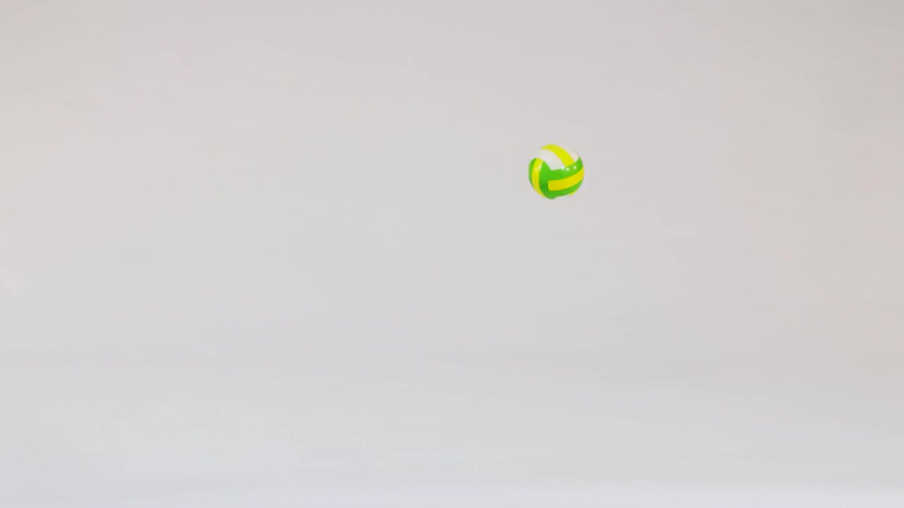 A small yellow and green volleyball bounces across a clean white studio background in slow-motion