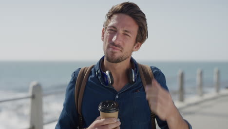 portrait-confident-young-man-running-hand-through-hair-enjoying-relaxing-on-ocean-seaside-holding-coffee-beverage-attractive-male-tourist-vacation-travel-slow-motion