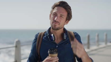 portrait confident young man running hand through hair enjoying relaxing on ocean seaside holding coffee beverage attractive male tourist vacation travel slow motion