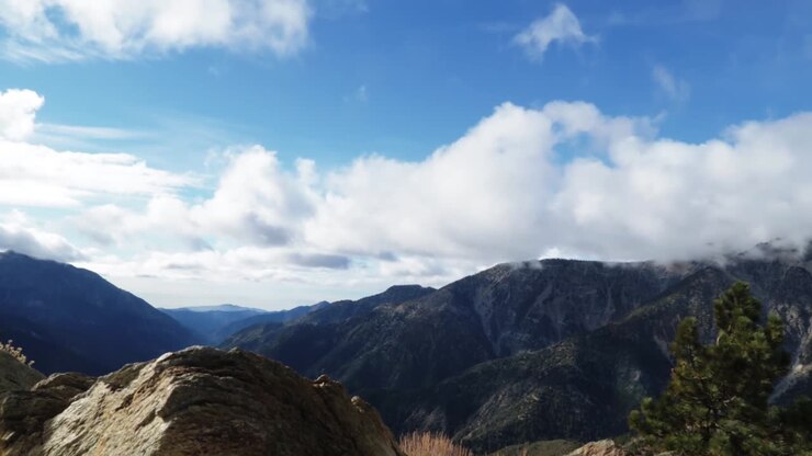 Montaña al fondo con nubes pasando en timelapse y una gran roca en primer plano.