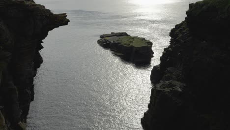 a lone rocky islet surrounded by cliffs in scotland, under soft evening light