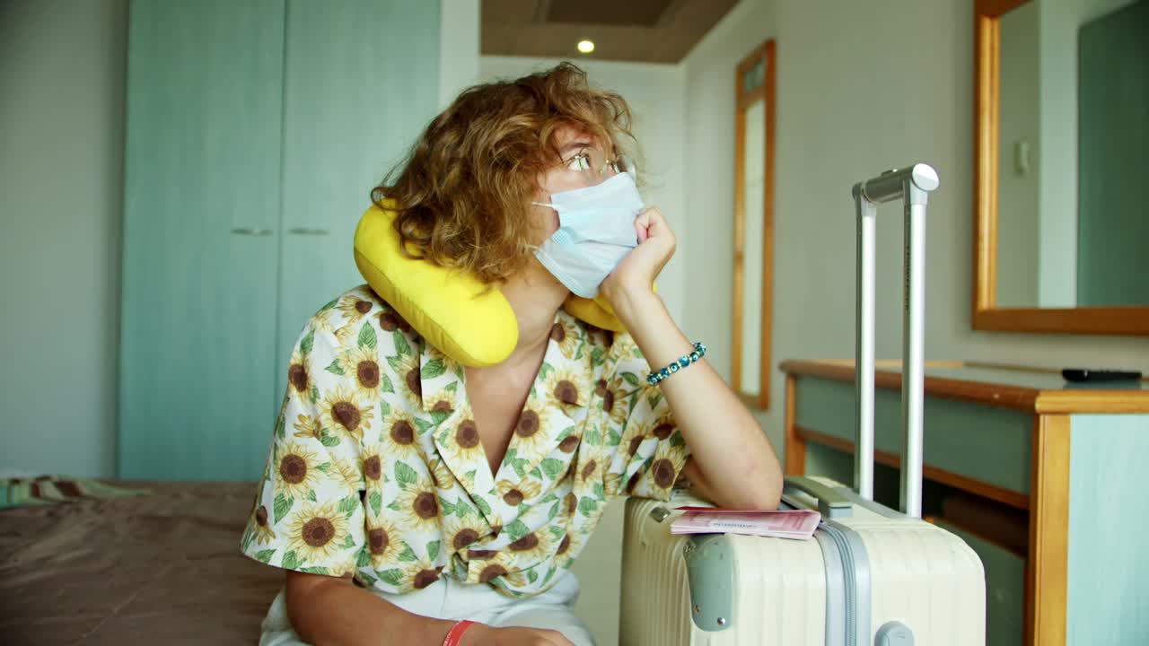 un turista desesperado molesto en problemas se sienta en una habitación de hotel en una cama no sabe qué hacer auto-aislación en un hotel en desesperación una máscara protectora el vuelo está cancelado cuarentena soledad agarra tu cabeza