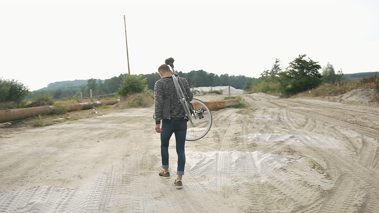 Uma pessoa carregando uma bicicleta em um ambiente arenoso ao ar livre