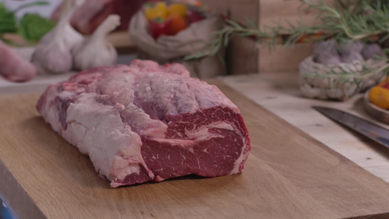 Close up of a butcher's hands placing a massive, highly marbled raw beef ribeye roast onto a wooden cutting board in a rustic kitchen