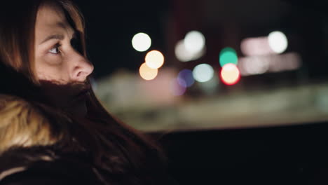 a woman sitting in a car at night, surrounded by blurred city lights. captured with a handheld camera, the scene highlights the urban nightlife and reflective mood