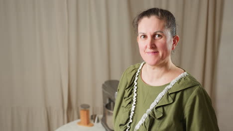 woman in green ruffled gown standing beside electric mixer, looking at camera with soft smile before shifting gaze upward, warm kitchen atmosphere with table and utensils in background