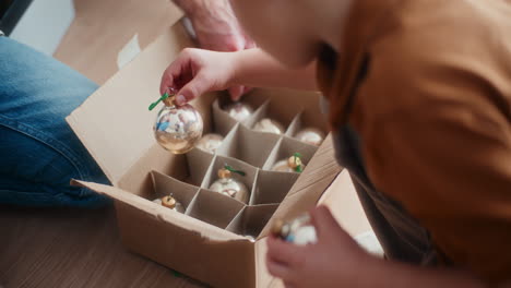 young boy looks at glass christmas baubles while decorating christmas tree