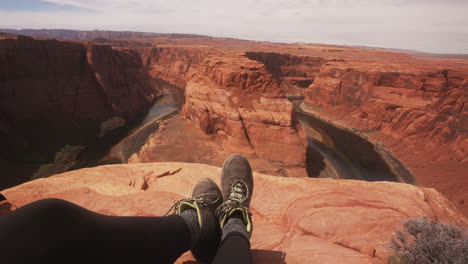 young woman hiker pov sitting above horseshoe bend in the grand canyon arizona, usa