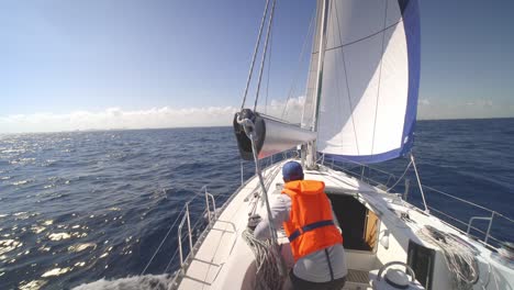 back of male in sailboat working on sails with rope and winch with tropical sea horizon in background, full frame