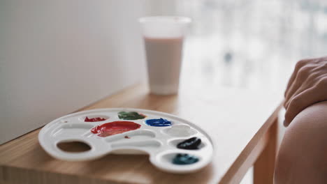 woman takes green paint from palette sitting near easel