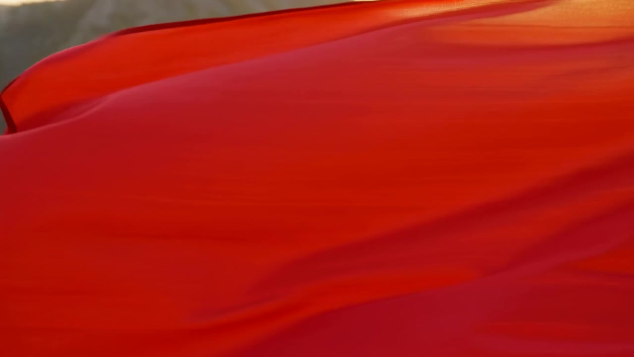 Red silk fabric fills foreground and midground, flowing into layered folds with raised ridge, soft sheen, diagonal creases, rich texture and warm hillside light for elegant dramatic visual effect