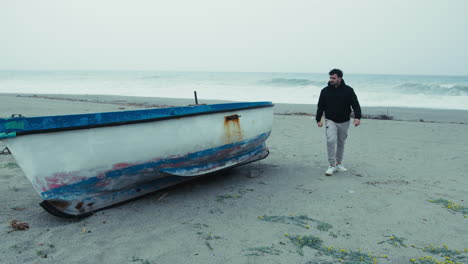 man at the winter sea leans on a boat to read a book