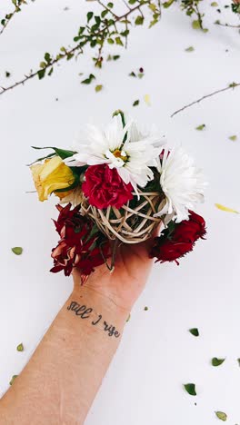 hand holding a small bouquet of mixed flowers with a 'still i rise' tattoo