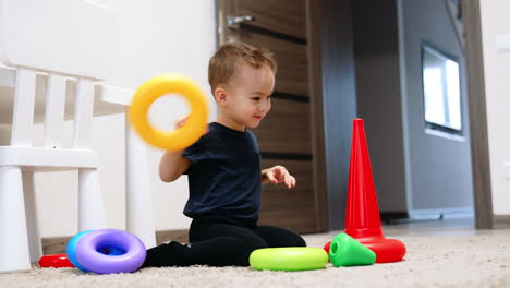 lovely smiling baby building a pyramid at home. cute child sitting on the floor plays with a toy.