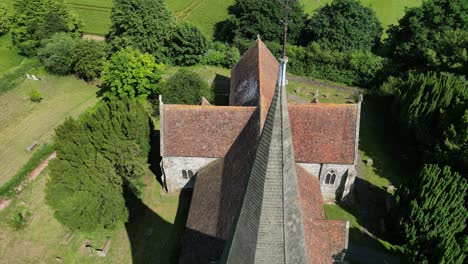 Steady-aerial-boom-shot-of-the-the-spire-of-St-John-the-Evangelist-church-in-Ickham,-Kent,-with-greenery-in-the-background