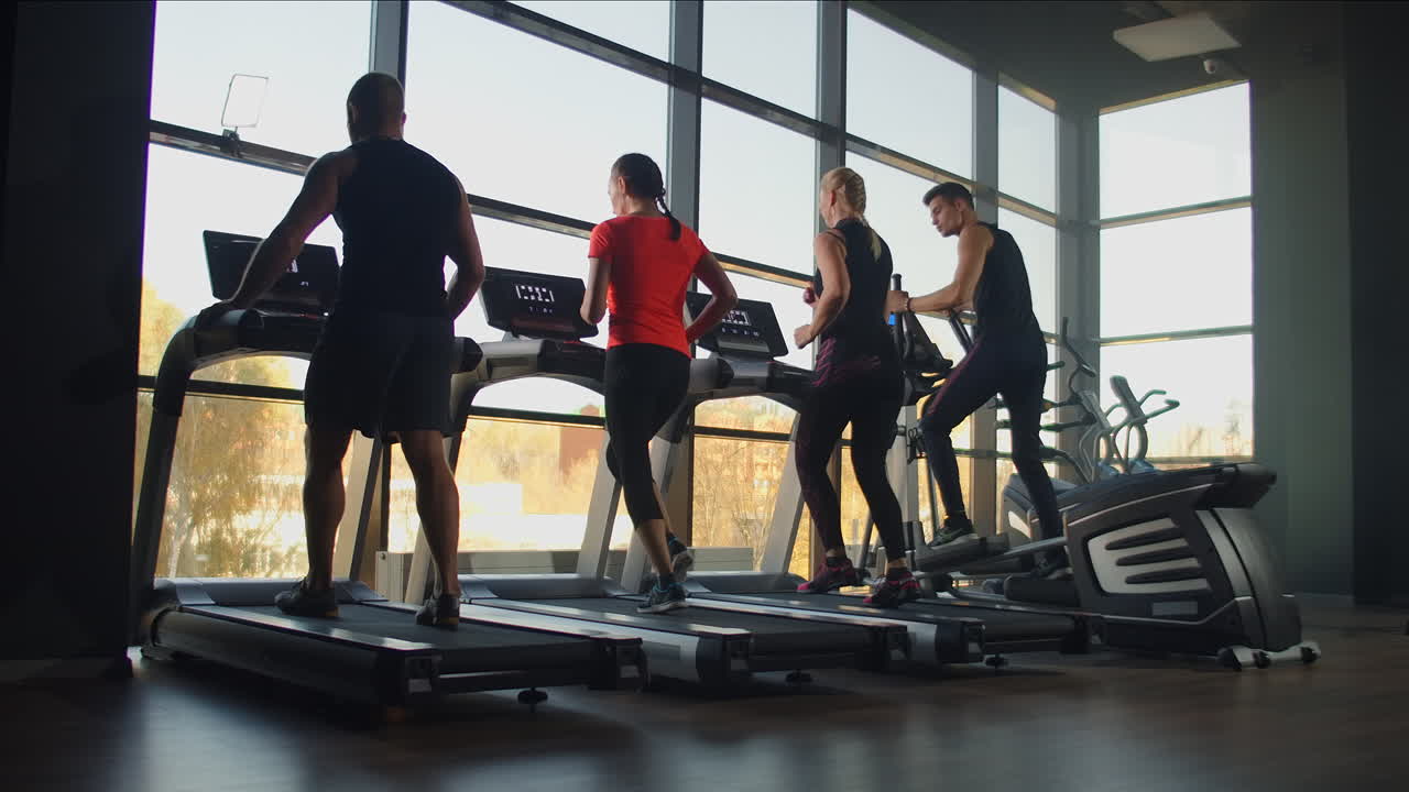 피트니스 클럽에서 트레드밀 기계에서 함께 달리는 피트니스 커플. 잘생긴 남자가 피트니스클럽에서 러닝 머신에서 여자를 훈련시니다. 뒷면