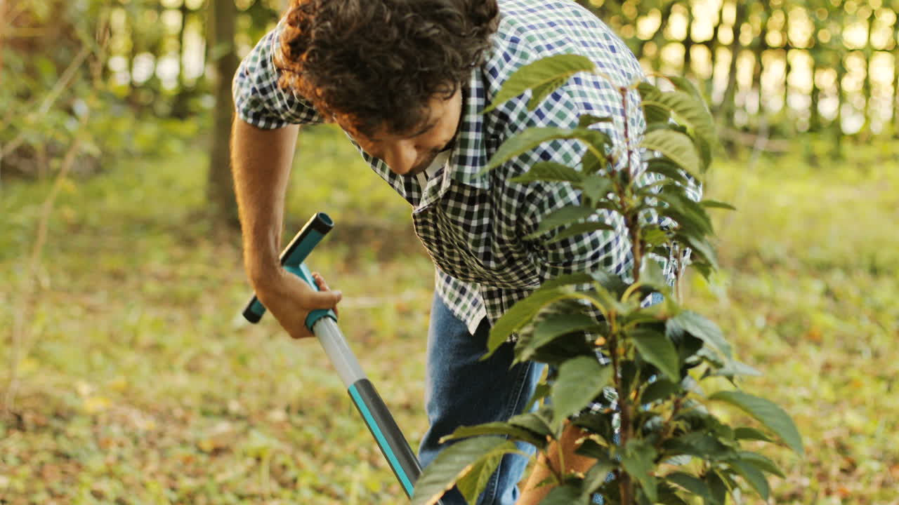 Closeup. Portrait of a farmer planting a tree. He uses the spade to put soil onto the roots. Then he stands up and smiles. Blurred background