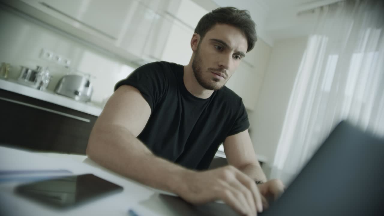 Uomo serio che digita al computer portatile a casa. Uomo d'affari che usa il computer in cucina