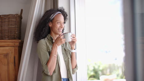 woman enjoying coffee by window at home, relaxing and looking outside, copy space