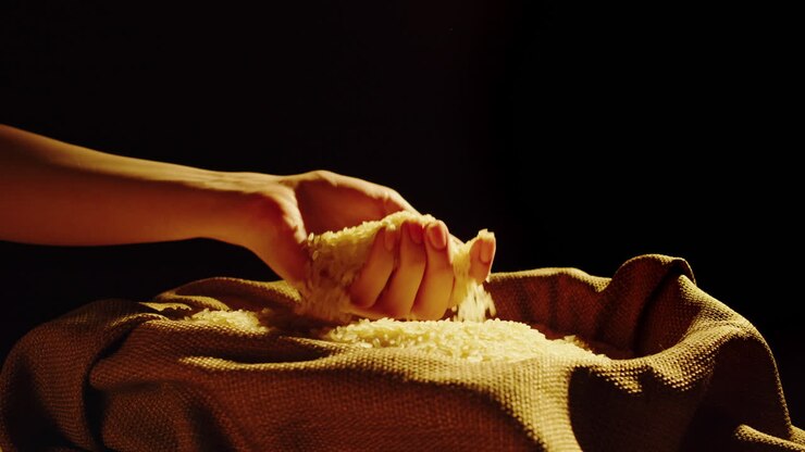A hand scooping and pouring rice grains from a burlap sack